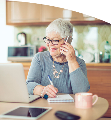 An older lady on the phone while using a laptop computer